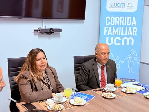 En una reunión, dos personas presentan información sobre la Corrida Familiar UCM mientras disfrutan de un desayuno.