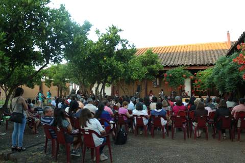 Un grupo de personas sentadas en sillas rojas en un entorno al aire libre rodeado de árboles y plantas.