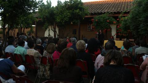 Una multitud de personas sentadas en sillas frente a un escenario en un ambiente al aire libre.