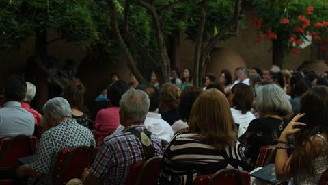 Una multitud de personas sentadas en un evento al aire libre rodeado de vegetación.
