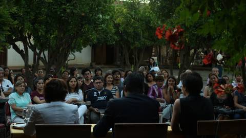Un grupo de personas sentadas en un evento al aire libre, observando a los ponentes en un escenario.