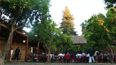 Una reunión al aire libre con muchas personas sentadas en sillas rojas, rodeadas de árboles en un ambiente natural.