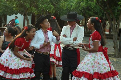 Un grupo de niños vestidos con trajes tradicionales interactuando y sonriendo en un ambiente festivo.