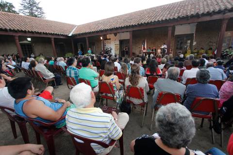 Una multitud de personas sentadas en sillas en un evento al aire libre con un escenario al fondo.