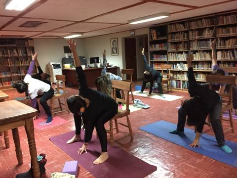 Un grupo de personas practicando yoga en un salón con estanterías llenas de libros.