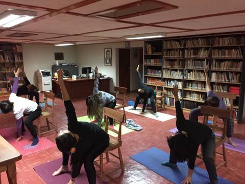 Un grupo de personas realiza yoga en una sala con sillas y estanterías llenas de libros.