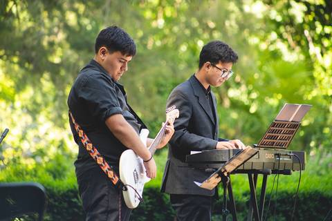 Dos jóvenes músicos actuando al aire libre, uno tocando la guitarra eléctrica y el otro en un teclado.