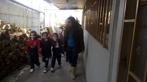 Un grupo de niños pequeños camina por un pasillo junto a una mujer adulta.