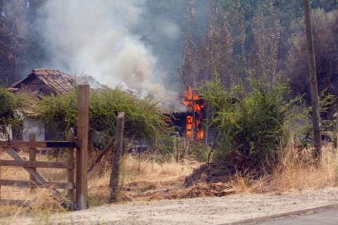 Una casa en llamas en medio de un paisaje seco y rural.