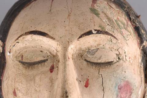 La imagen muestra un rostro escultórico con detalles de pintura desgastada y ojos cerrados.