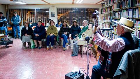 Un grupo de personas escucha a un hombre que toca la guitarra en una biblioteca.