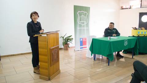 Una mujer está dando un discurso frente a una audiencia en un evento formal.