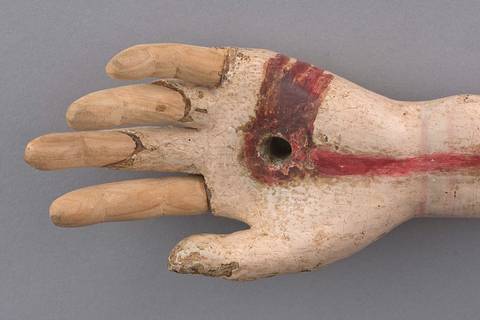 Una mano tallada en madera con un agujero en el centro de la palma y marcas en color rojo.