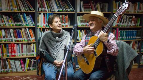 Una pareja de personas disfruta de un momento musical en un ambiente acogedor de biblioteca.