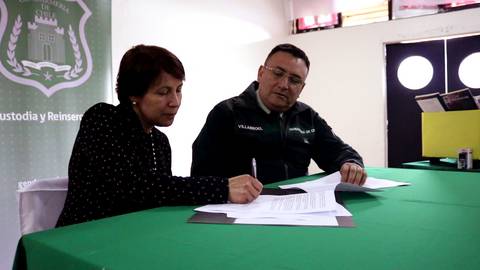 Un hombre y una mujer están firmando documentos sobre una mesa verde.