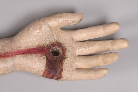 Una mano de modelo artístico con un agujero en la palma y pintura roja en la muñeca.