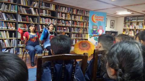 Dos narradoras cuentan historias a un grupo de niños en una biblioteca.