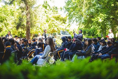 Un grupo de estudiantes sentados en sillas al aire libre, rodeados de árboles y un ambiente natural.