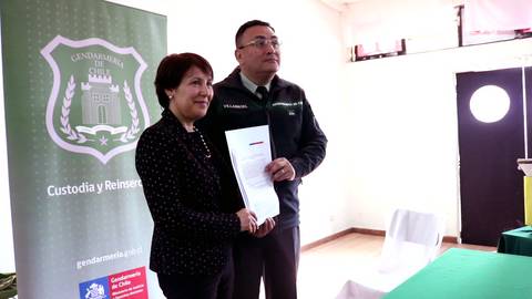 Una mujer y un hombre posan juntos sosteniendo documentos en un evento relacionado con Gendarmería en Chile.