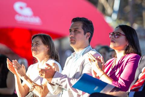 Un grupo de personas aplaudiendo durante un evento al aire libre bajo un paraguas rojo.