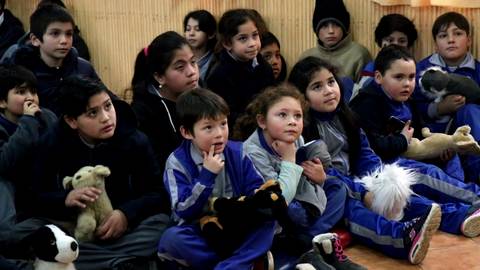 Un grupo de niños sentados en un aula, atentos y sosteniendo peluches.