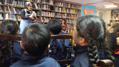 Un grupo de niños escucha atentamente a una narradora en una biblioteca.