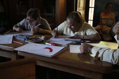 Un grupo de personas mayores dibujando en una mesa en una biblioteca.