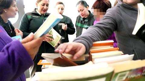 Un grupo de mujeres examinan libros en una mesa durante un evento de intercambio literario.
