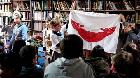 Un grupo de niños presenta una bandera en una biblioteca durante una actividad cultural.
