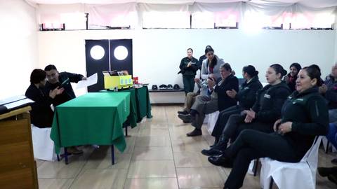 Una reunión con personas sentadas en sillas frente a una mesa verde.