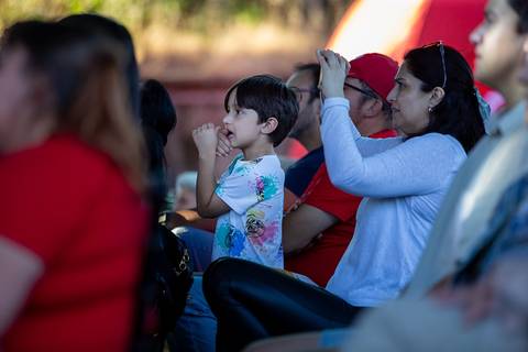 Un grupo de personas observa atentamente un evento al aire libre mientras un niño las mira con interés.