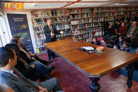 Una conferencia se lleva a cabo en una biblioteca con un público atento y un orador en el centro.