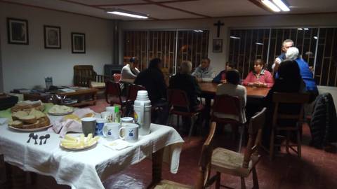 Un grupo de personas reunidas alrededor de una mesa en un ambiente acogedor con comida y bebidas.