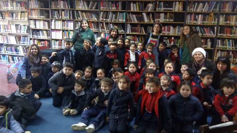 Un grupo de niños y adultos sonríen juntos en una biblioteca rodeados de estanterías llenas de libros.