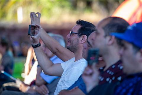 Un grupo de personas sentadas en un evento, algunas de ellas grabando con sus teléfonos móviles.