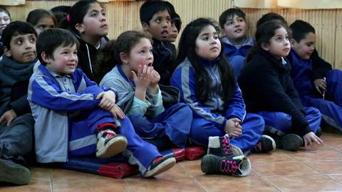 Un grupo de niños sentados en el suelo, mirando atentamente hacia adelante.