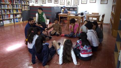 Un grupo de niños y un adulto se sientan en círculo en una biblioteca mientras participan en una actividad grupal.