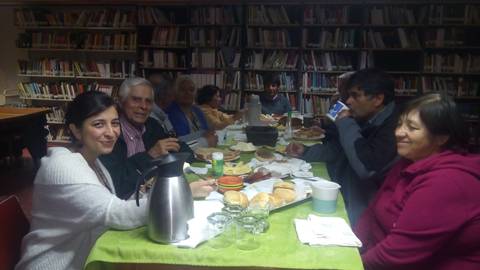 Un grupo de personas comparte una comida en una mesa rodeada de estanterías llenas de libros.