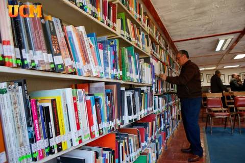 Un hombre está revisando libros en una estantería de una biblioteca.