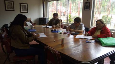 Un grupo de personas sentadas alrededor de una mesa en una sala, trabajando en sus cuadernos.