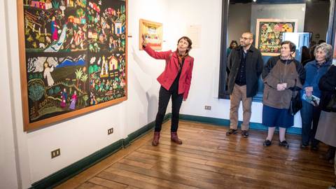 Una guía explica una obra de arte en una galería mientras los visitantes escuchan atentamente.