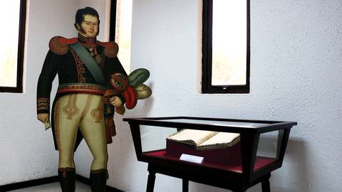 Un retrato en tamaño real de un soldado de la independencia mexicana con un libro antiguo en una vitrina.