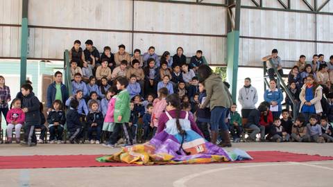 Un grupo de niños observa un espectáculo en un gimnasio escolar mientras otros se preparan para participar.