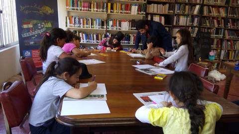 Un grupo de niños y adultos trabajando en una actividad creativa en una biblioteca.