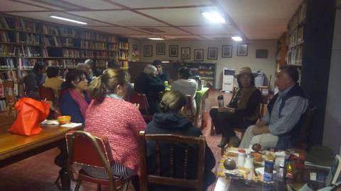 Un grupo de personas está sentado en una sala acogedora rodeada de estanterías llenas de libros, participando en una conversación.