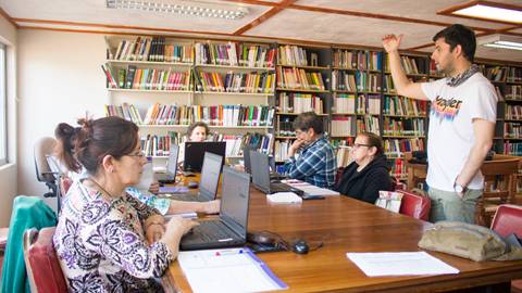 Un grupo de personas en una biblioteca asisten a una charla mientras un hombre se dirige a ellos.