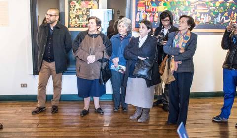 Un grupo de personas de pie en un ambiente interior, observando una obra de arte en la pared.
