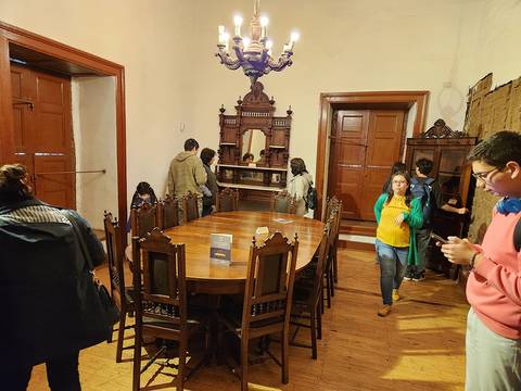 Una sala antigua con un comedor grande y personas observando el lugar.