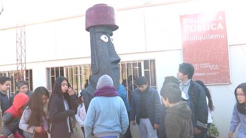 Un grupo de personas se reúne cerca de una escultura en la entrada de una biblioteca pública.