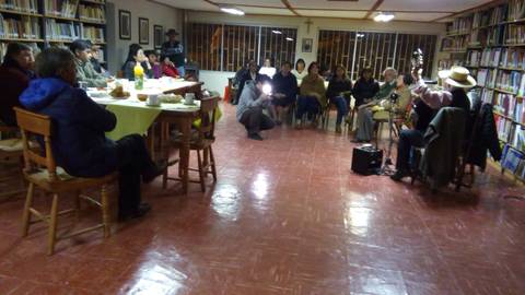 Un grupo de personas asiste a un evento cultural en una biblioteca, donde un músico toca la guitarra.